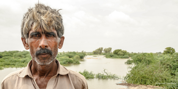 A serious looking older man stands in flooded fields.