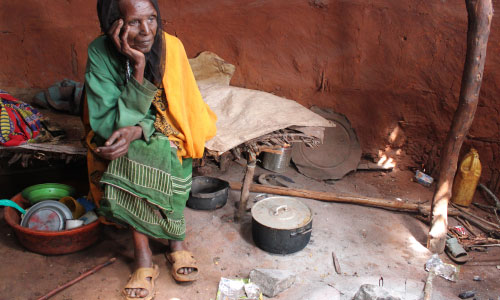 An older woman in Ethiopia sits, head in hands, in her home